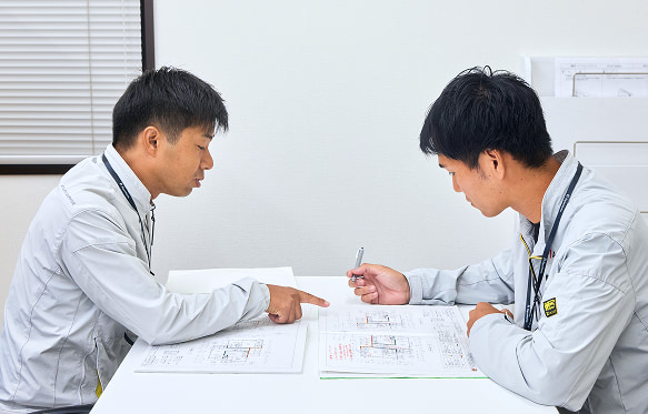 工務店のスタッフが新築の注文住宅の設計図面を確認し、高品質な戸建住宅の自由設計について相談している様子です。